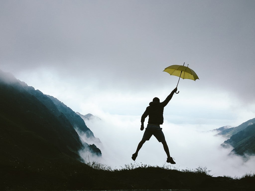 hiker in midair holding a yellow umbrella