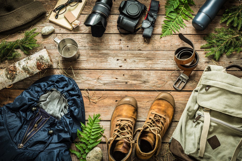rustic gear arranged on wooden table showcasing hiking boots, camera and backpack 