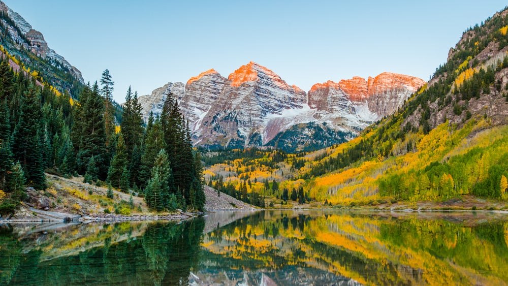 Orange alpenglow on Maroon Bells mountaintops reflect in alpine lake