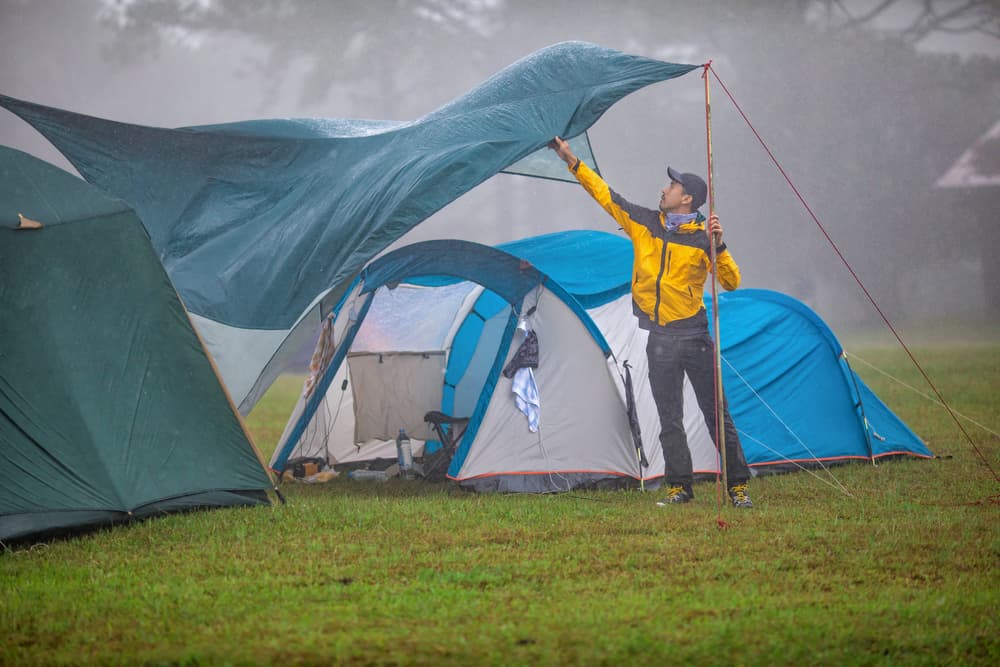 camper tries to set up tarp between two tents during windy rainstorm