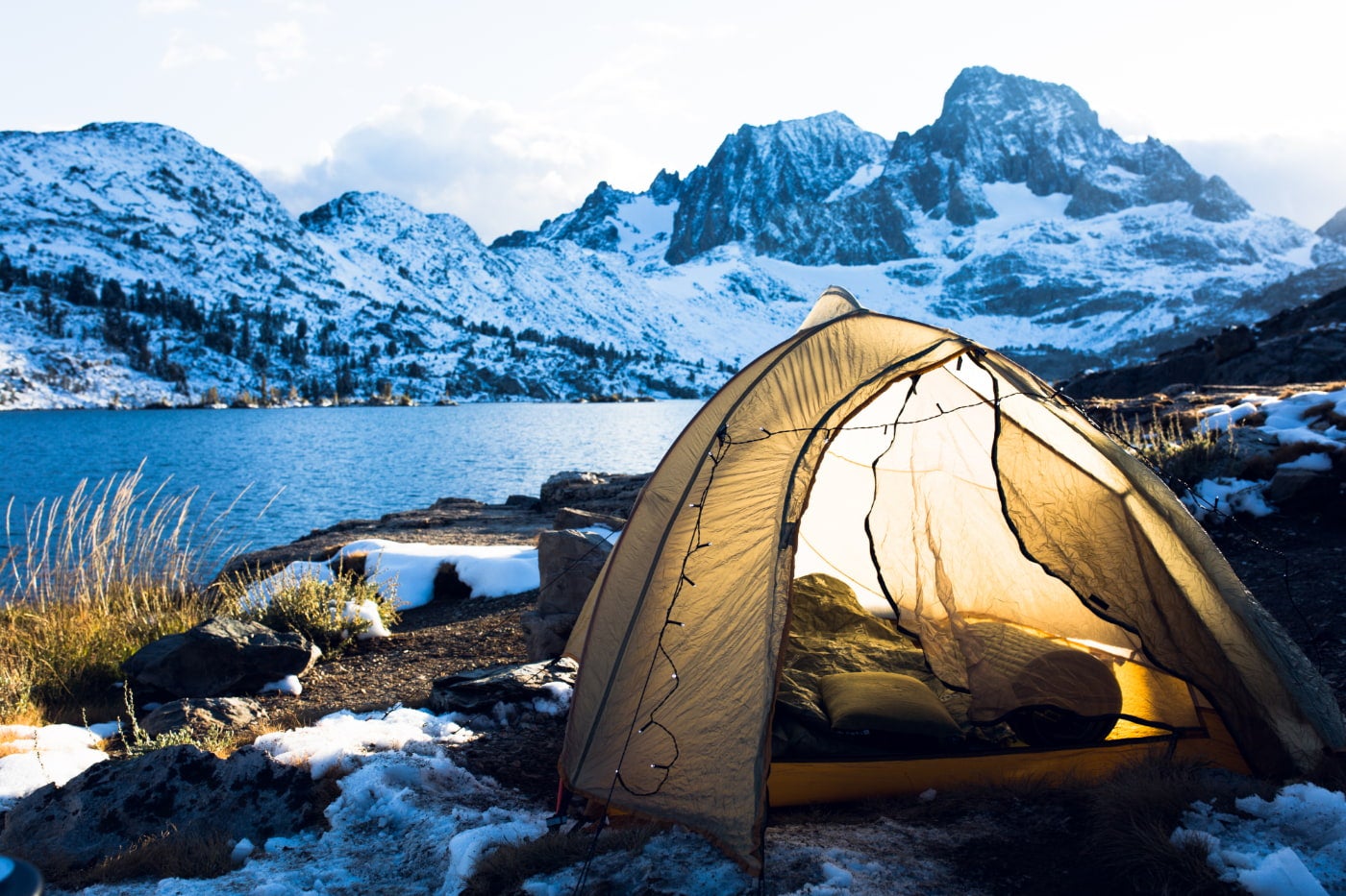 lights draped over yellow tent in waterfront campsite near alpine lake