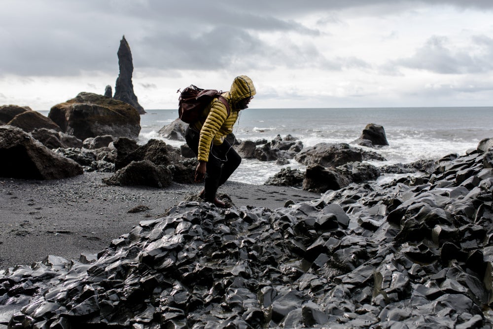 Man in yellow coat climbing on rocks at a black sand beach 