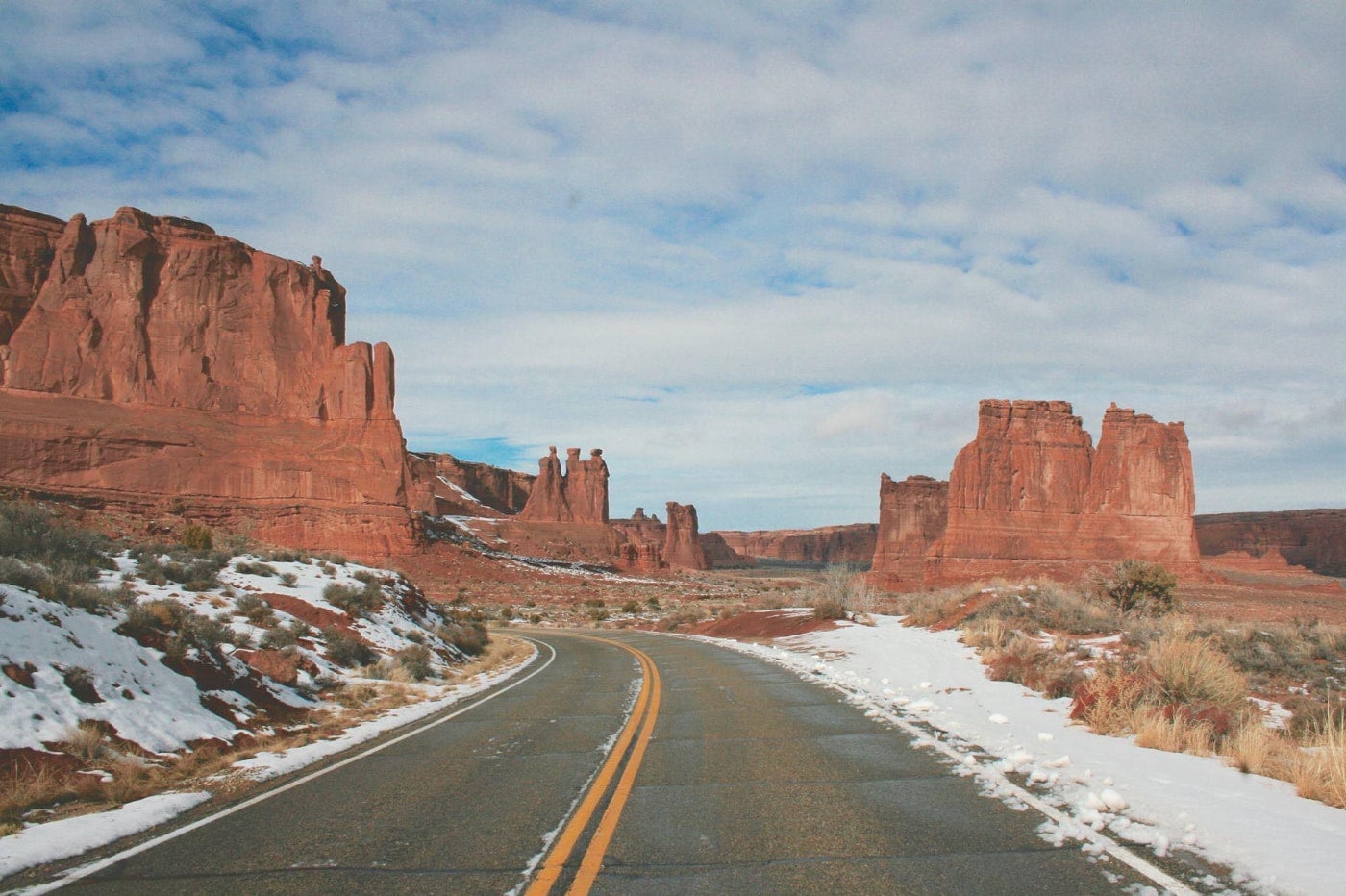 Two lane road winds through the snow-dusted desert in arches national park surrounded by red rock formations