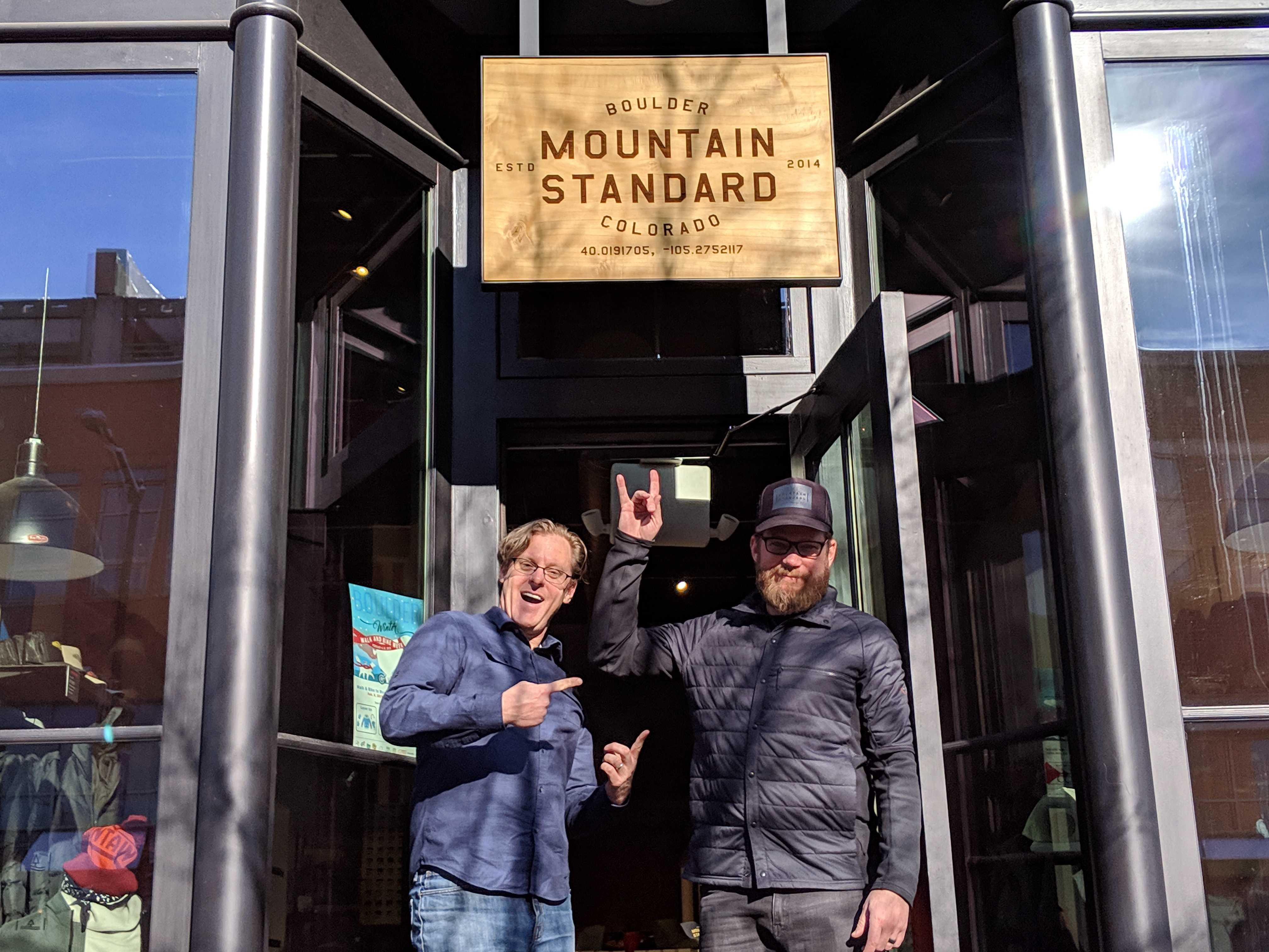 two men post for photo beneath mountain standard storefront 