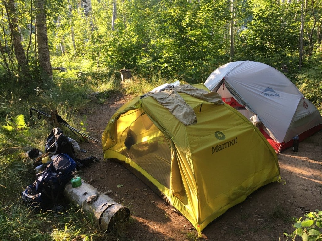 two tents set up beside one another in a wooded campsite as gear rests outside