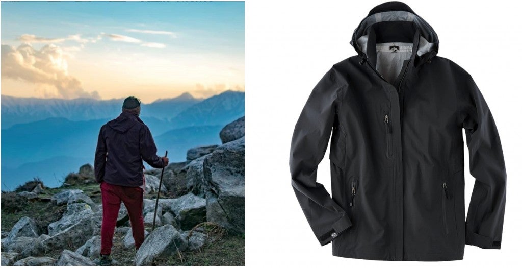 a black rain jacket is seen worn by a man climbing a mountain with the hood tucked in, and also seen unworn with the hood up