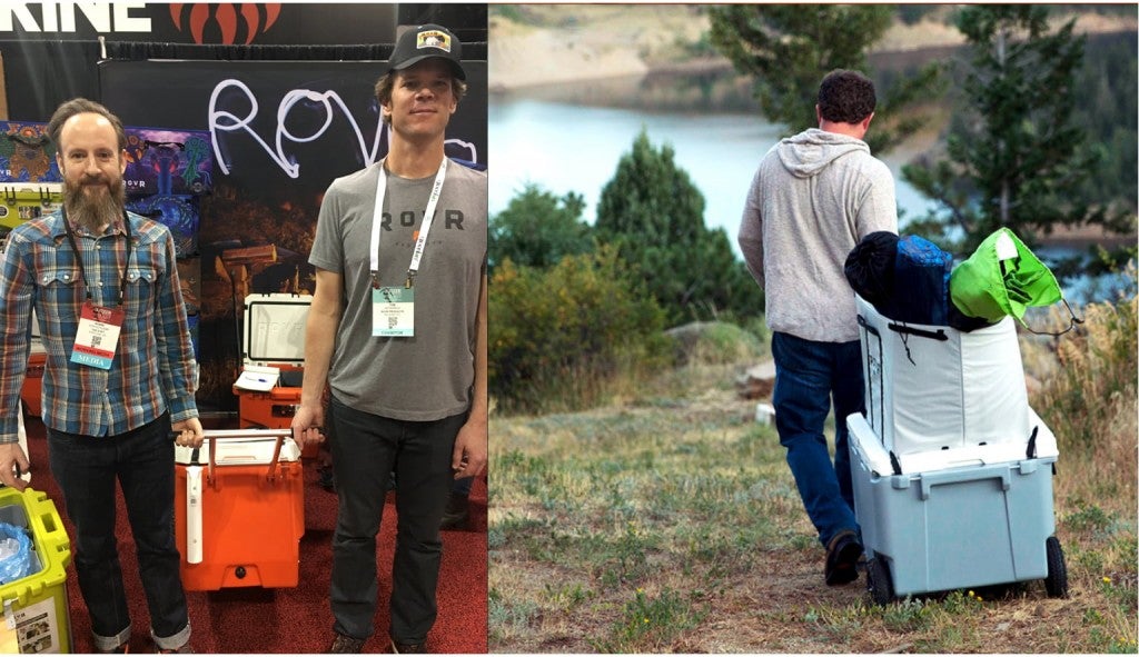 two men attending outdoor retailer hold a cooler by a handle (right) one man rolling a cooler down a hill filled with gear