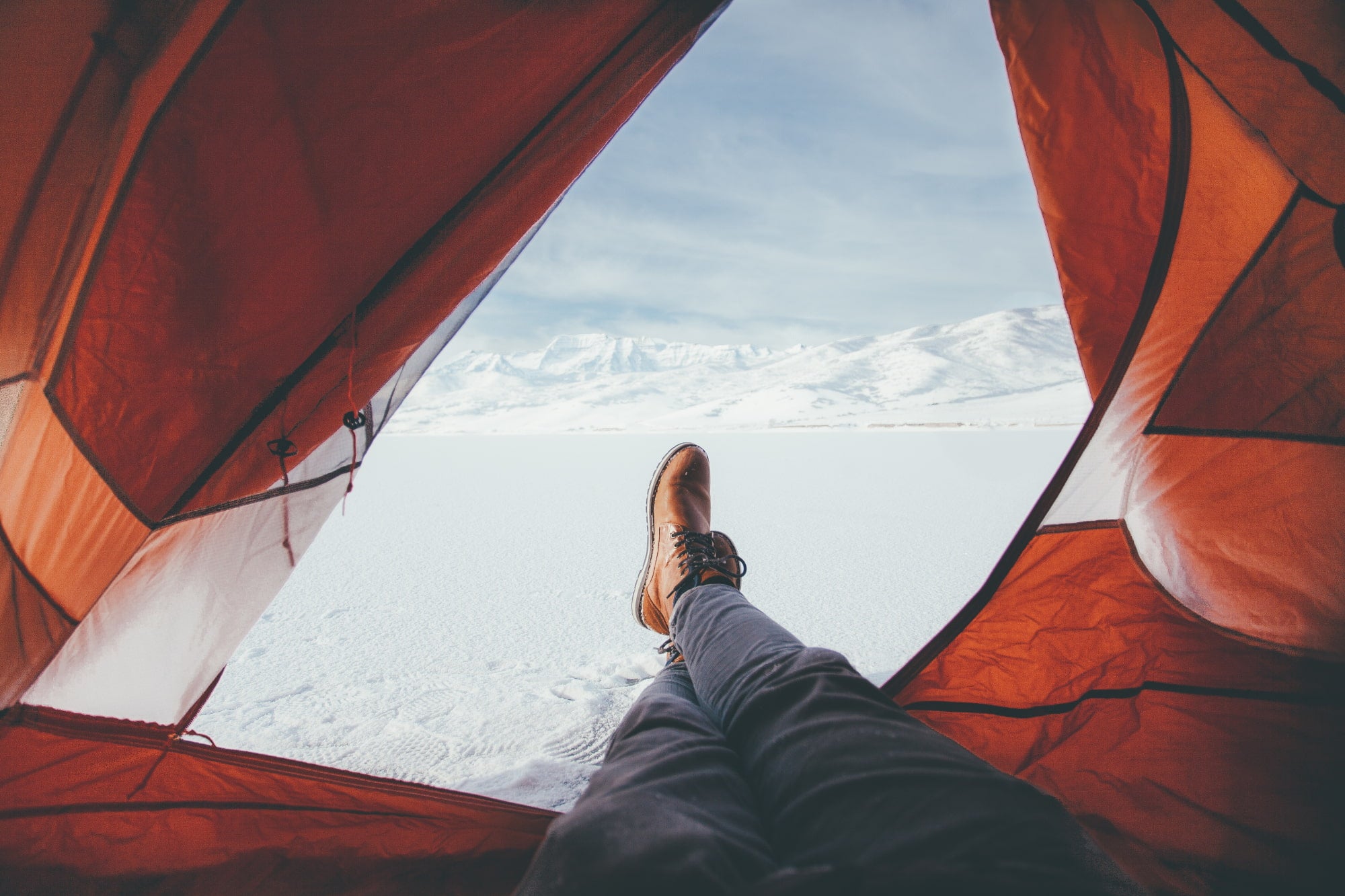 view from inside of tent showing a camper stretching his legs out of the door into a field of fresh snow