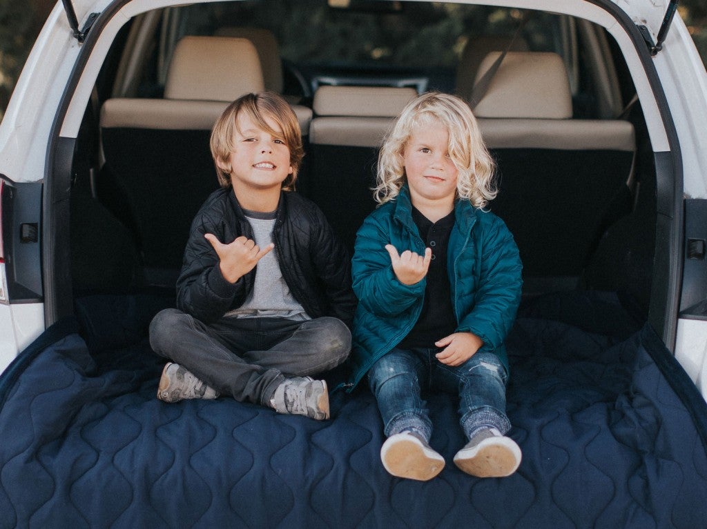 two young boys holding up shaka hand signs in the back of a camping suv