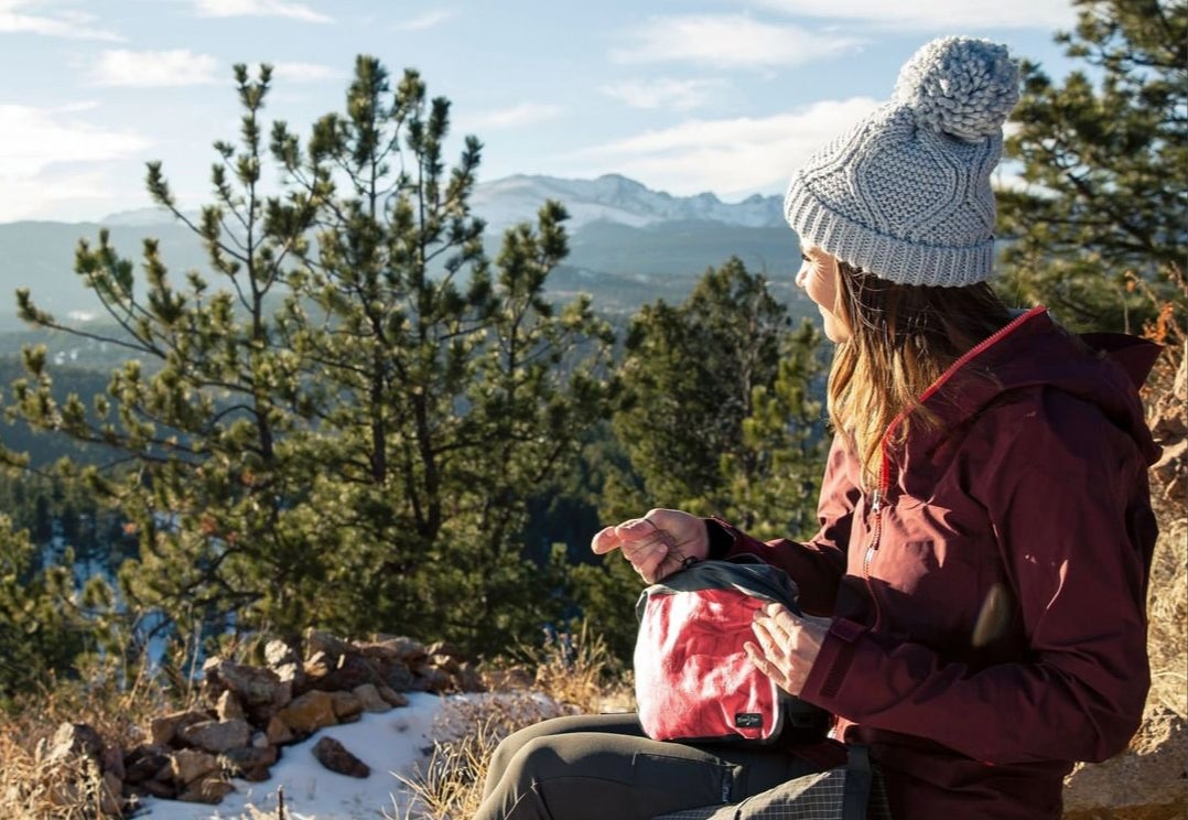 female hiker rests on scenic overlook and holds toiletry bag in hand