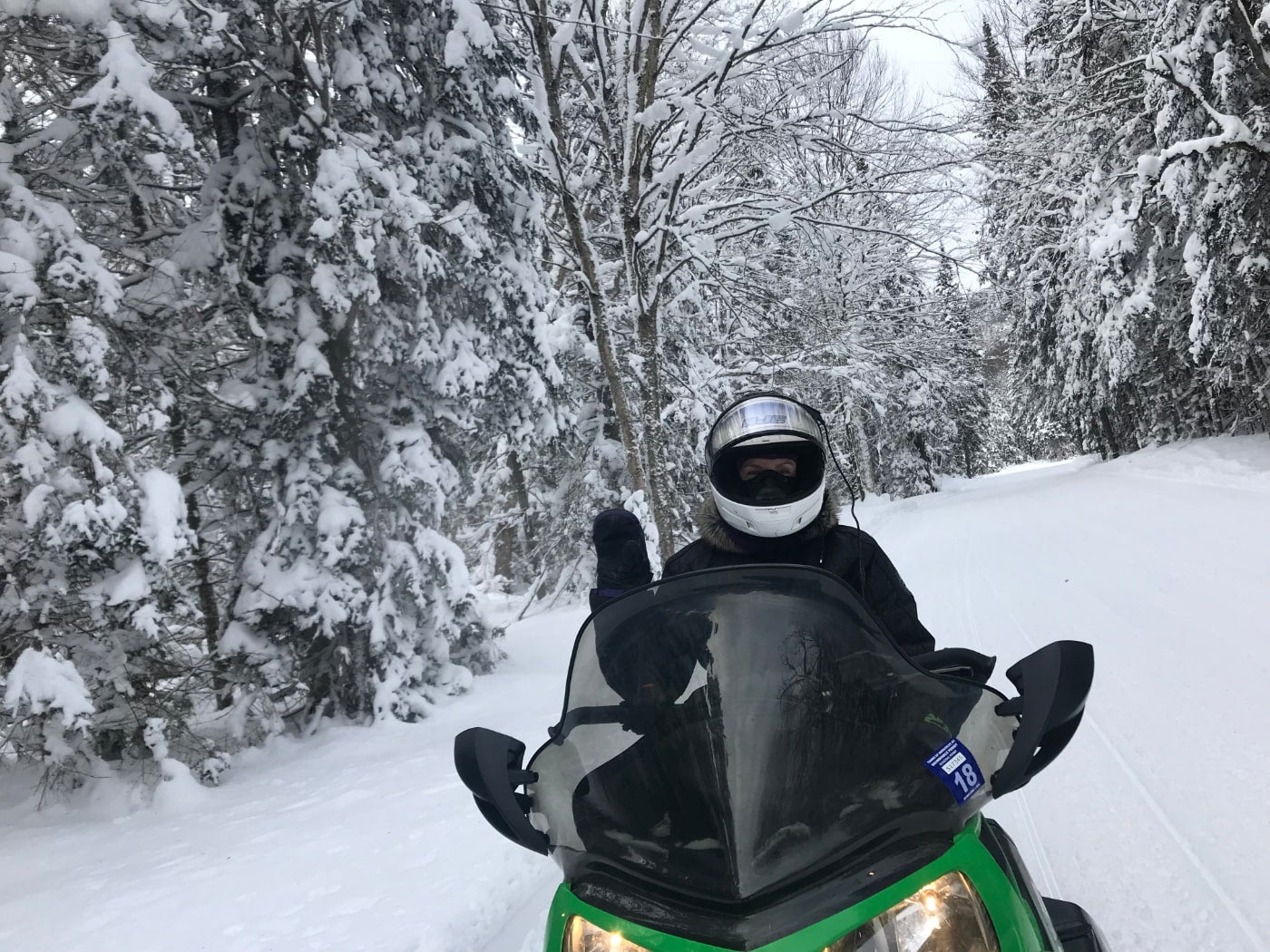 Person on snowmobile in a snow covered forested area waving to camera