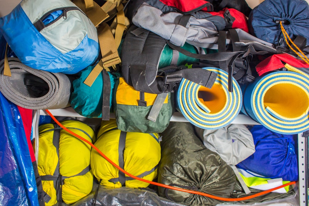 Camping gear including yellow tents, and orange sleeping pad, a black backpack, a green tarp, and more stacked in a large pile.