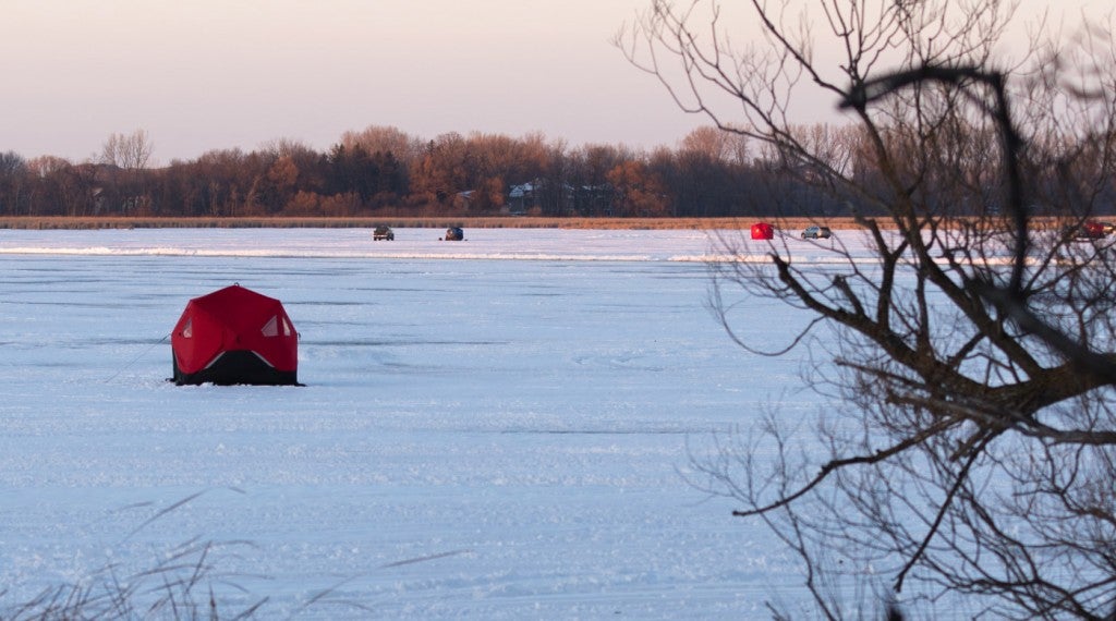a single red ice fishing tent sits on a frozen lake in minnesota with multiple ice fishing tents behind it