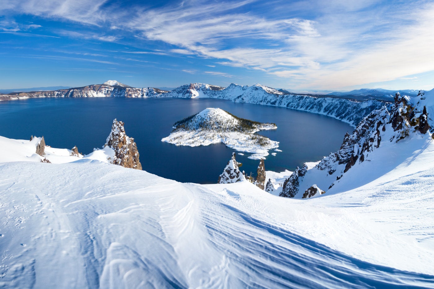 oregon's crater lake surrounded by a heavy layer of snow with Wizard island in the middle of the lake