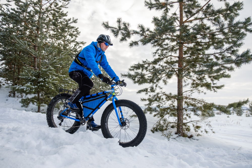 Winter cyclist on a fat bike passes trees as he rides downhill through the snow