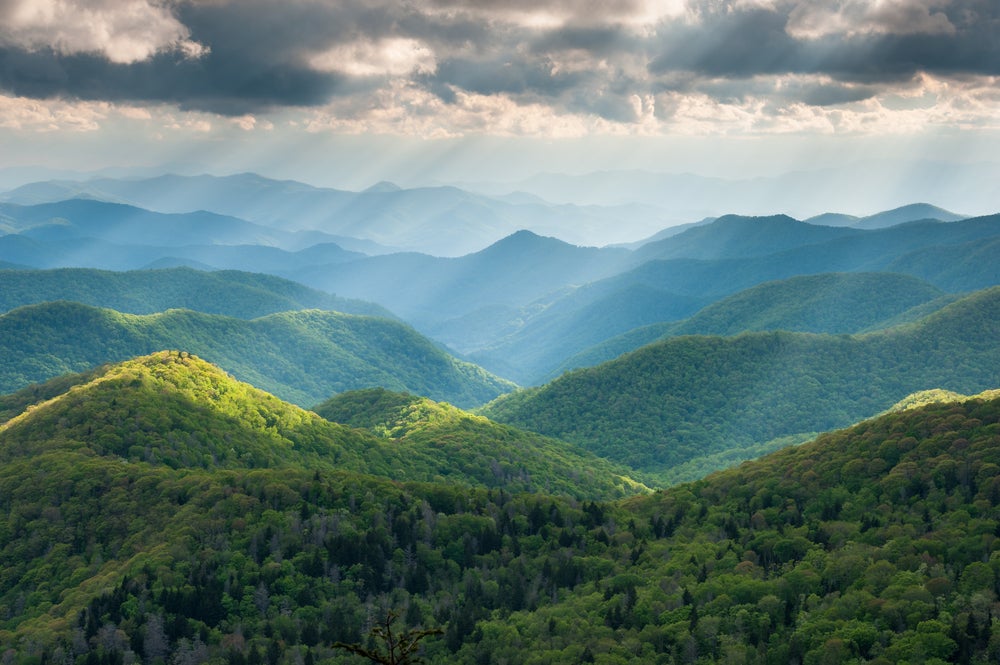 sun rays shine through clouds onto blue ridge mountains