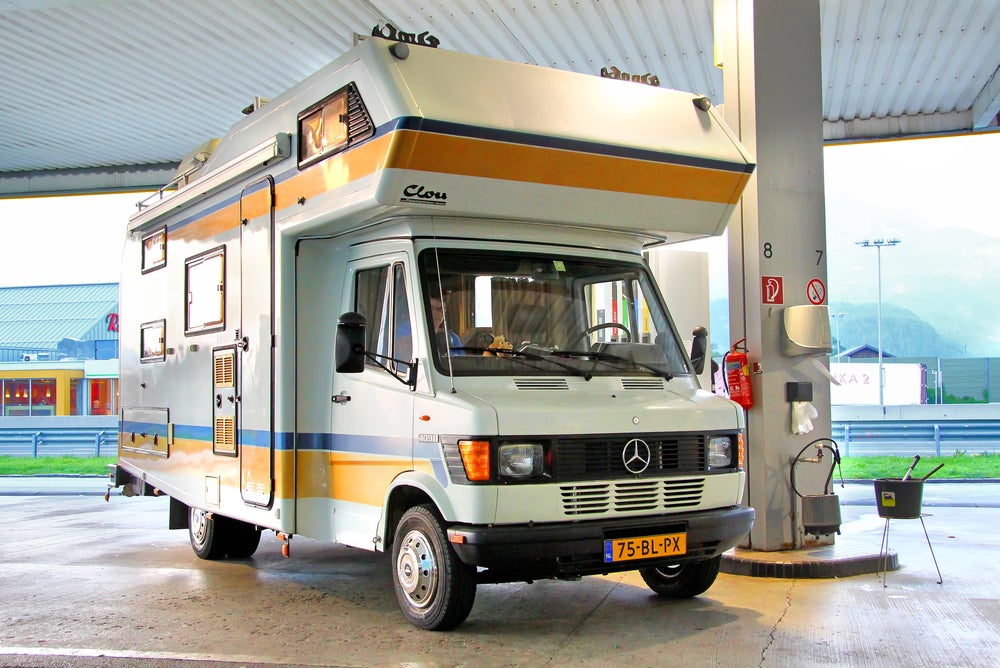 Old school yellow striped mercedes RV filling up at a gas station.