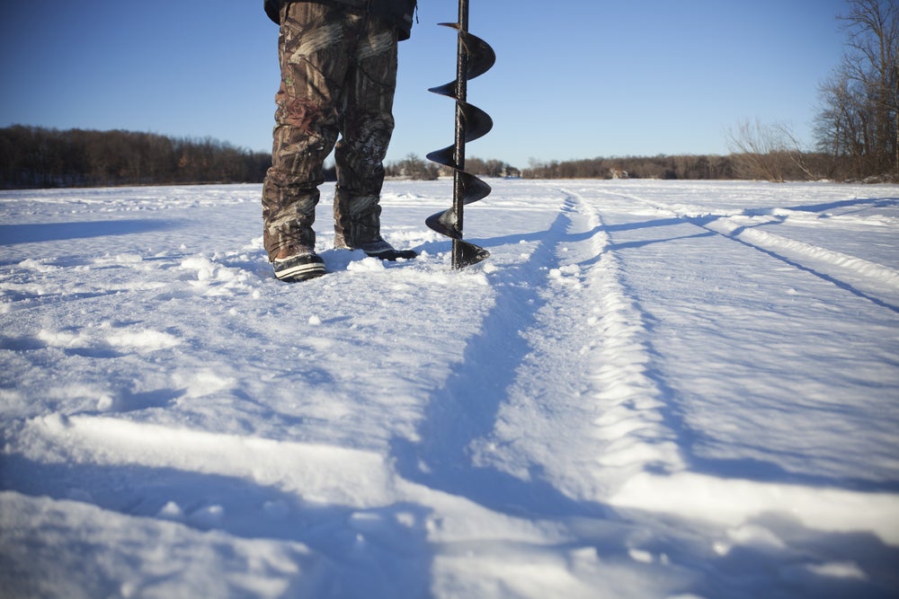 ground level view of man in winter gear preparing to drill ice fishing hole