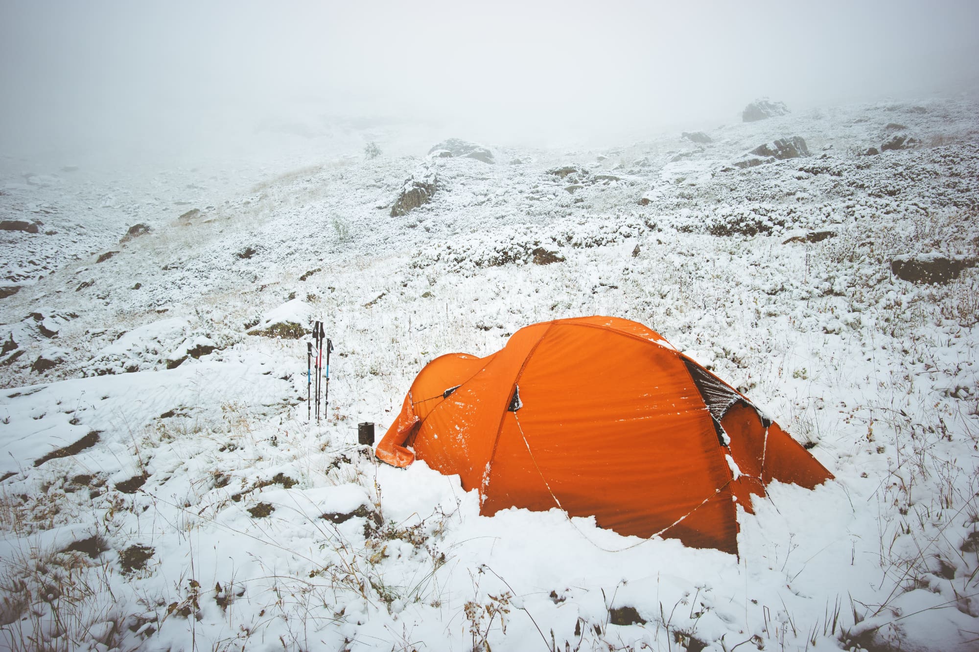 an orange tent rests on a snowy field in the middle of winter