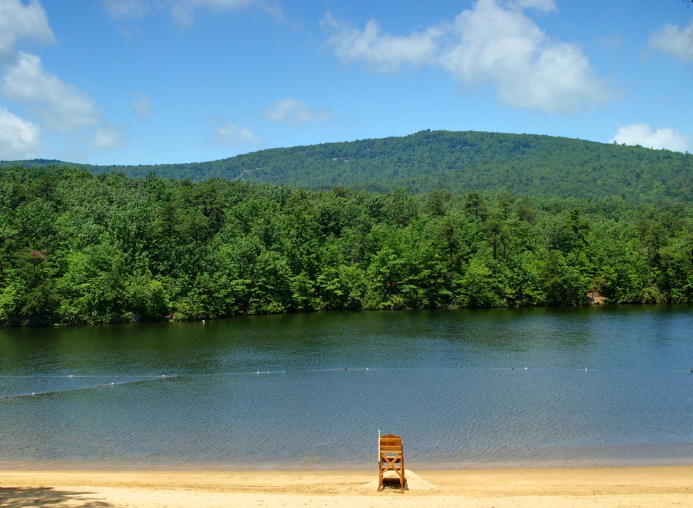 a lakeshore beach with a lifeguard chair at Hanging Rock State Park Lake, with rolling green woodlands in the background