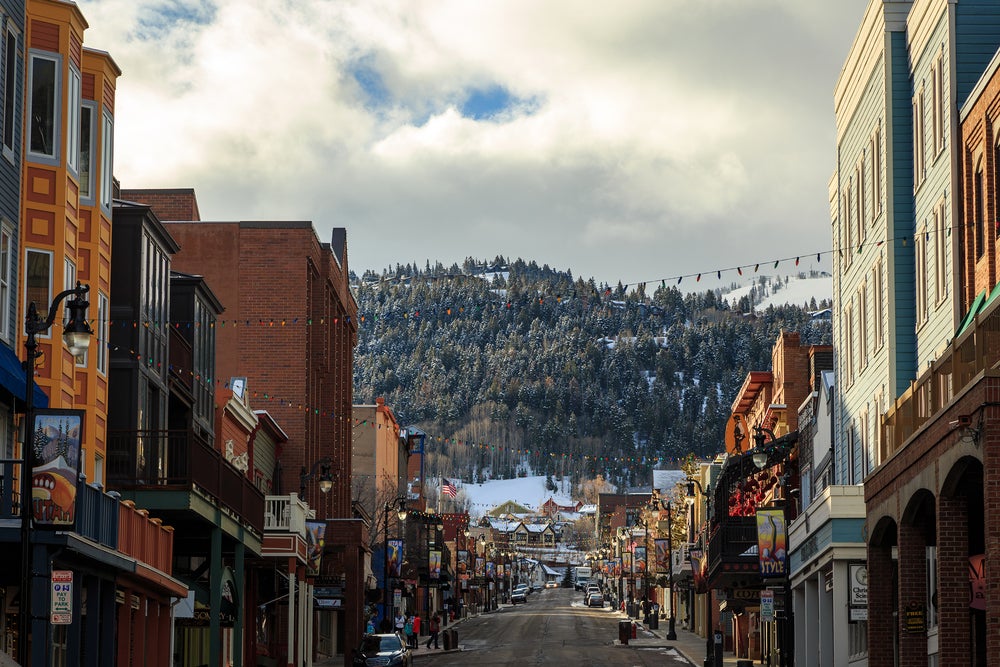 A street in downtown Park City Utah with colorful christmas lights strung in front of a snowy mountain