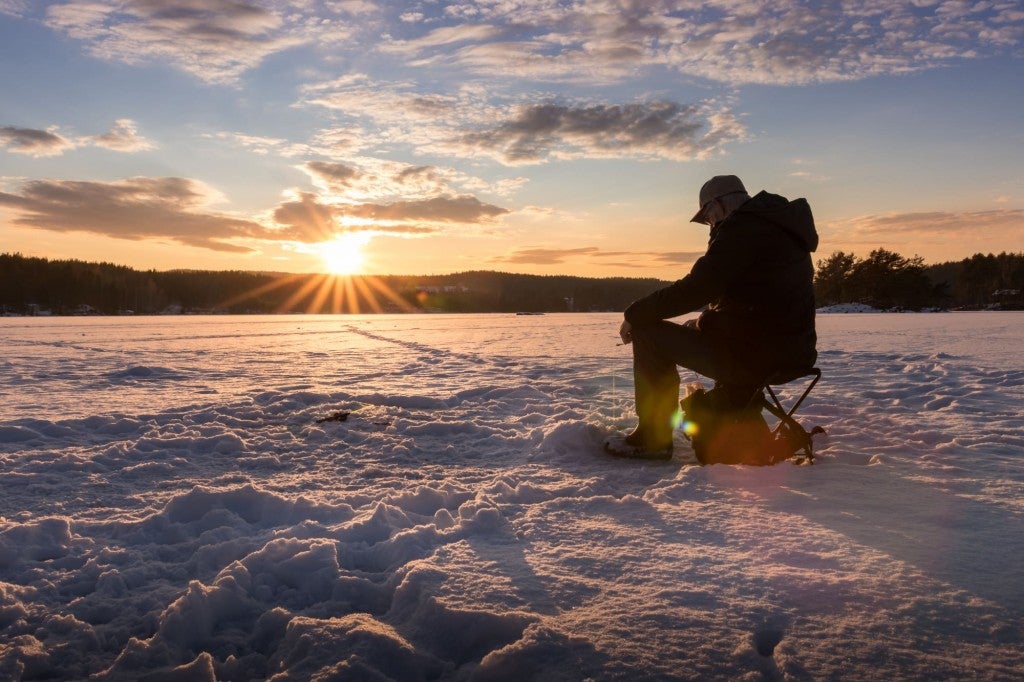 a silhouette of a person sits on a frozen lake while ice fishing in minnesota