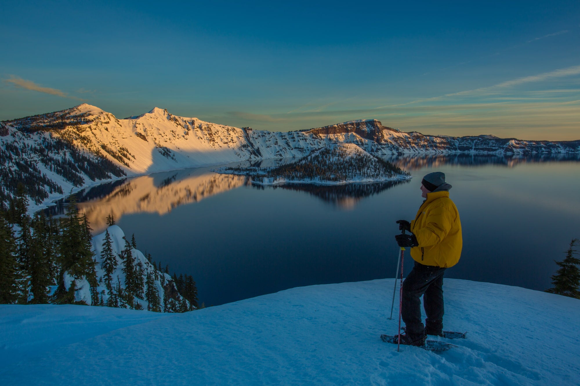 a man at a snowy overlook snowshoeing in crater lake national park at sunset