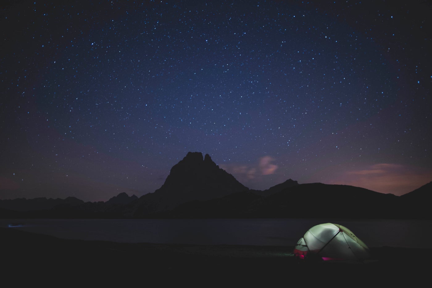 a tent with a light inside it on a silhouetted campsite under a purple and blue night sky