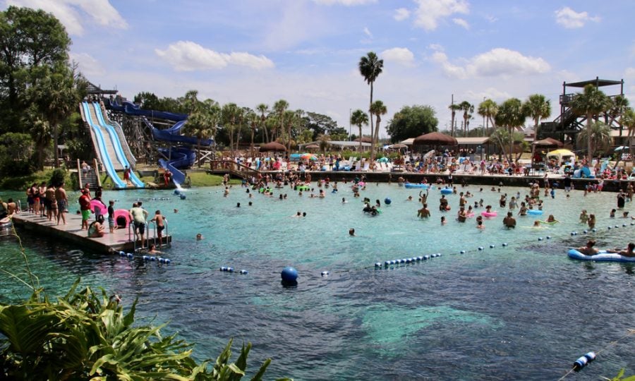 Panoramic view of water park with slides, bright blue water and palm trees in background 