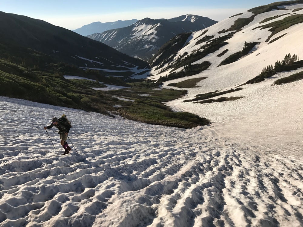 Man hiking up snowfield with valley and mountains behind him 
