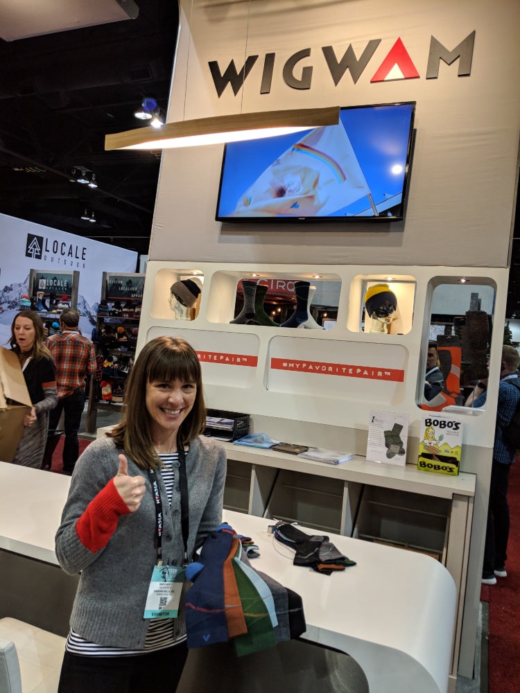 a woman smiles holding wigwam wool socks in front of a product booth