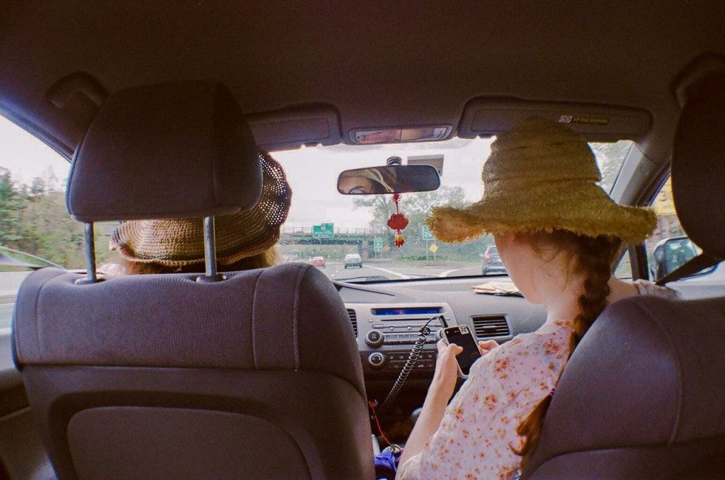 backseat view of two women in car as passenger searches for a road trip playlist on phone