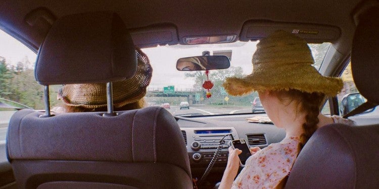 backseat view of two women in car as passenger searches for a road trip playlist on phone