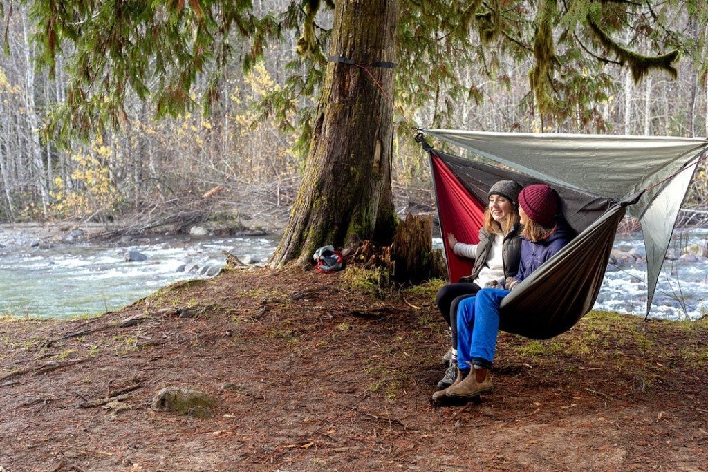 two women sit in a hanging 4-season hammock near a river in winter