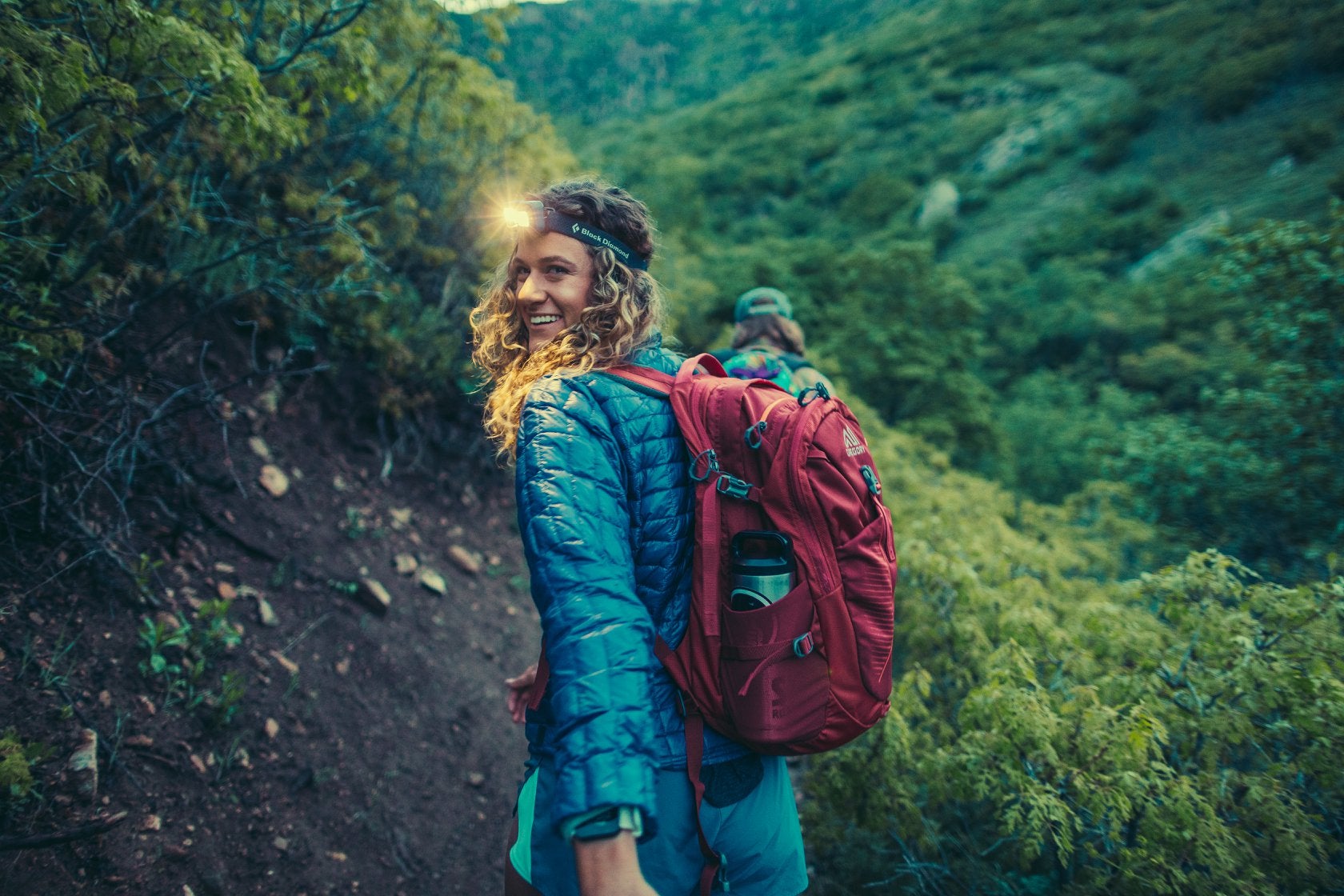 a woman wearing a headlamp and backpack hiking on a trail