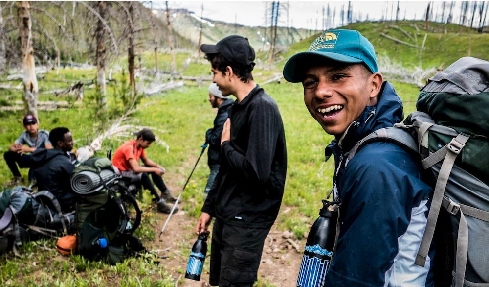 Laughing boy with several friends around him all backpacking in the mountains