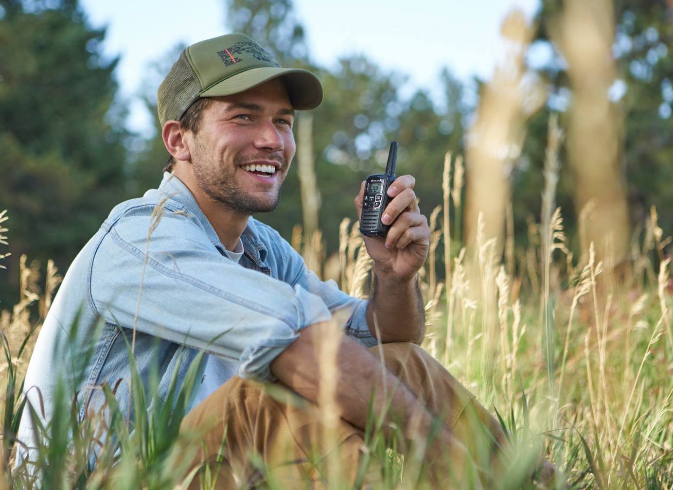 a man smiling in the woods holding a midland walkie talkie