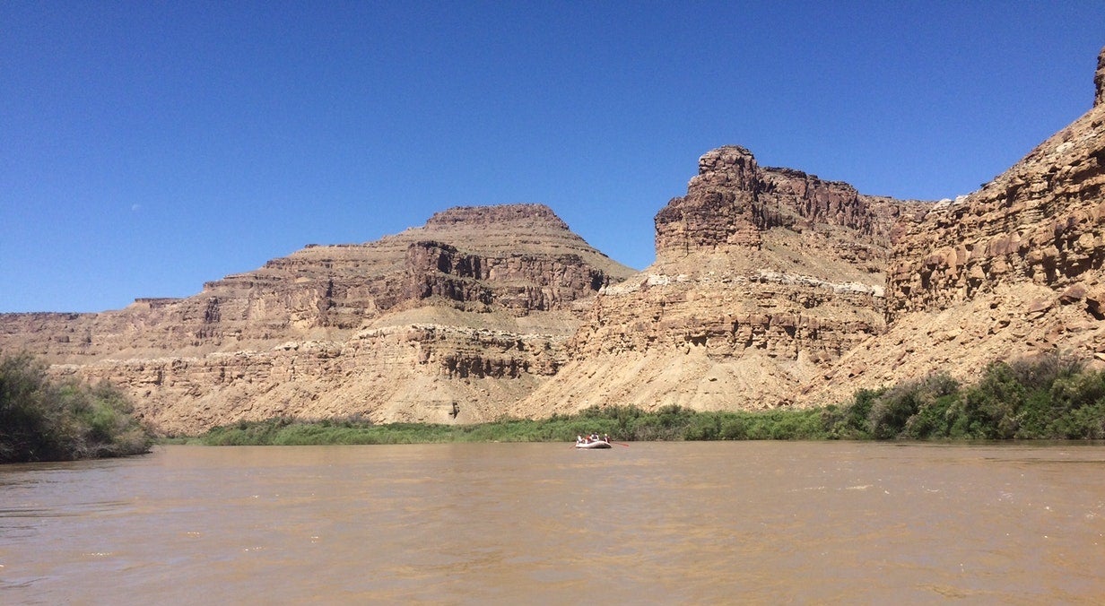 inflatable raft in the distance floats on muddy waters in utah desert