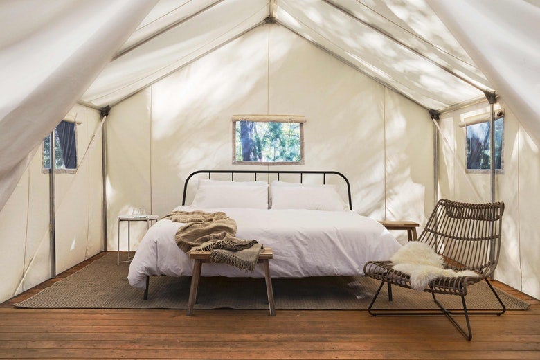 white bedding covers large bed inside of canvas glamping tent, featuring modern furniture and furs