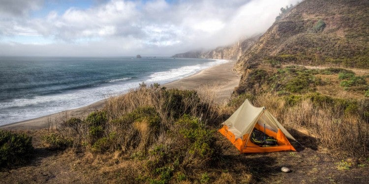 Orange tent set up in field above the north california coastline.