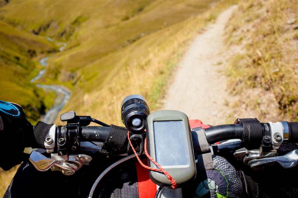 The handlebars of a bike packed with gear and a gps on a mountain trail.