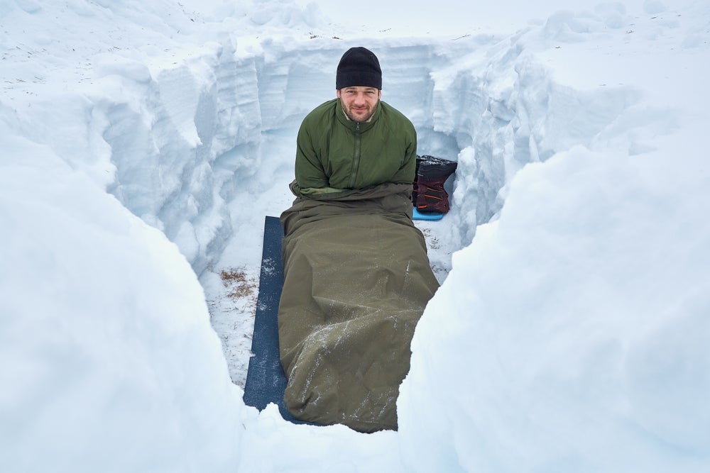 Man sleeping in dugout hole in snow.