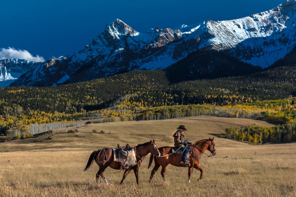 Rancher riding and leading a horse in the Colorado Rockies.