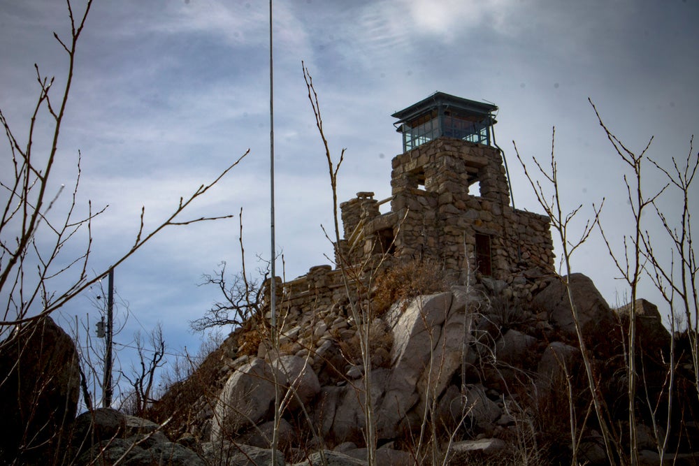 Bare trees frame a stone fire tower on rocky hill