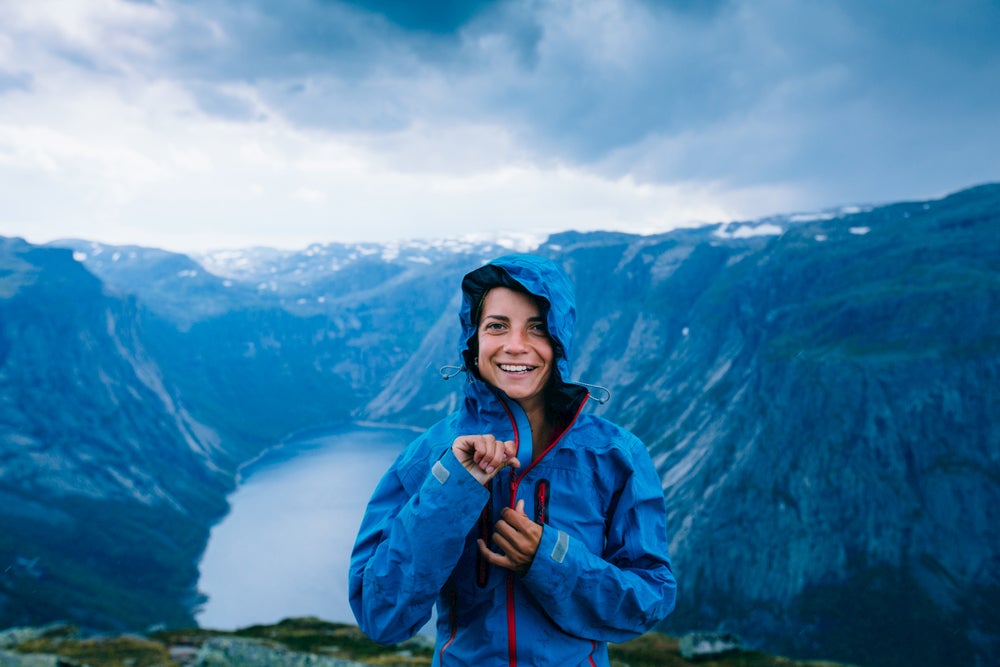 Woman smiling at camera and zipping up her jacket with alpine lake in background