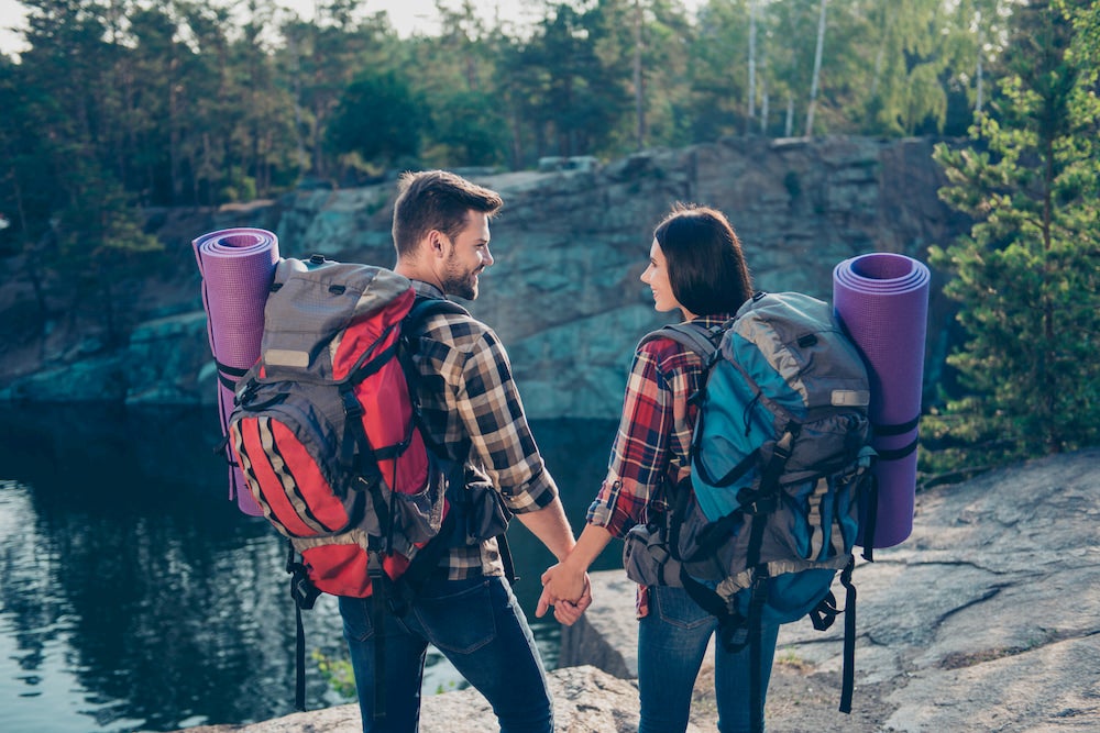 a couple on a backpacking trip wearing gear packs and romanticly holding hands in the wilderness