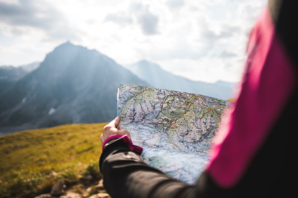 woman holding topographical map overlooking mountains