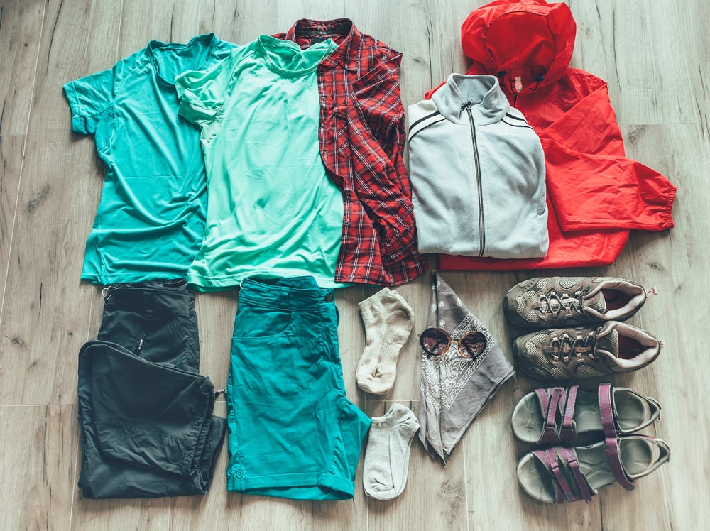 Folded hiking clothes including rain coat, shoes, base layer etc laid out on floor