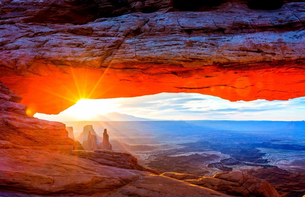 Arched red rock displaying open valley and red towers at sunrise
