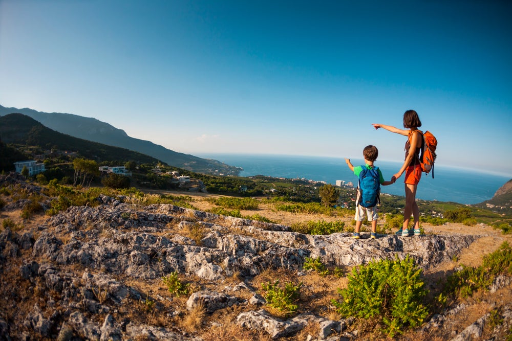 Mother and child hold hands while stopping to admire a coastal viewpoint during a hike.
